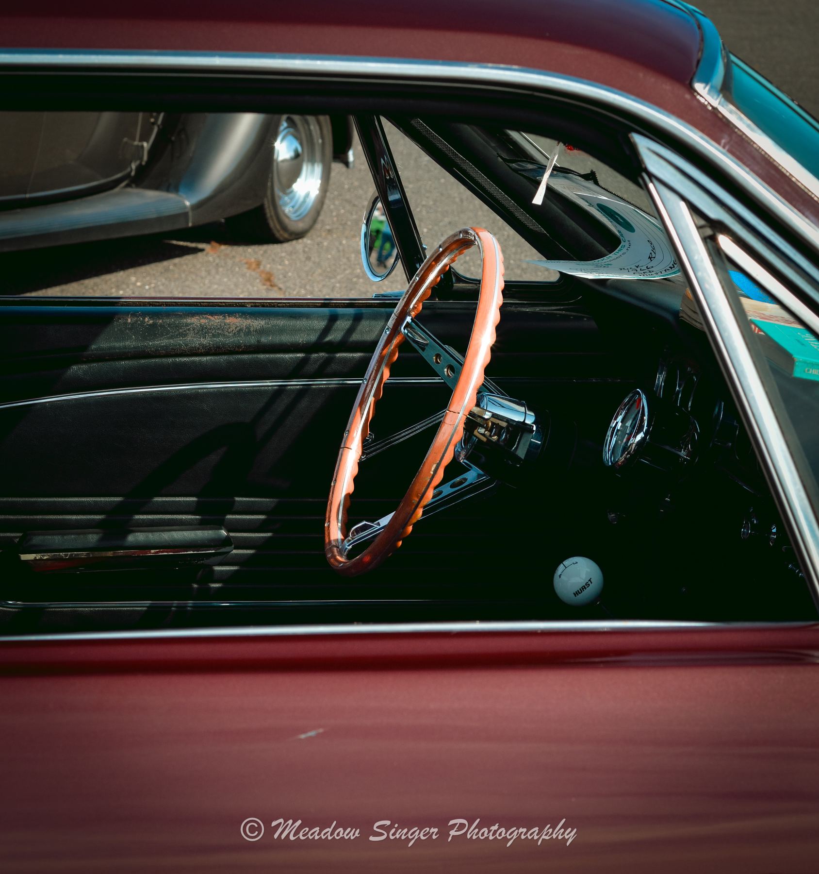 A wooden steering wheel inside a vintage car with deep red paint