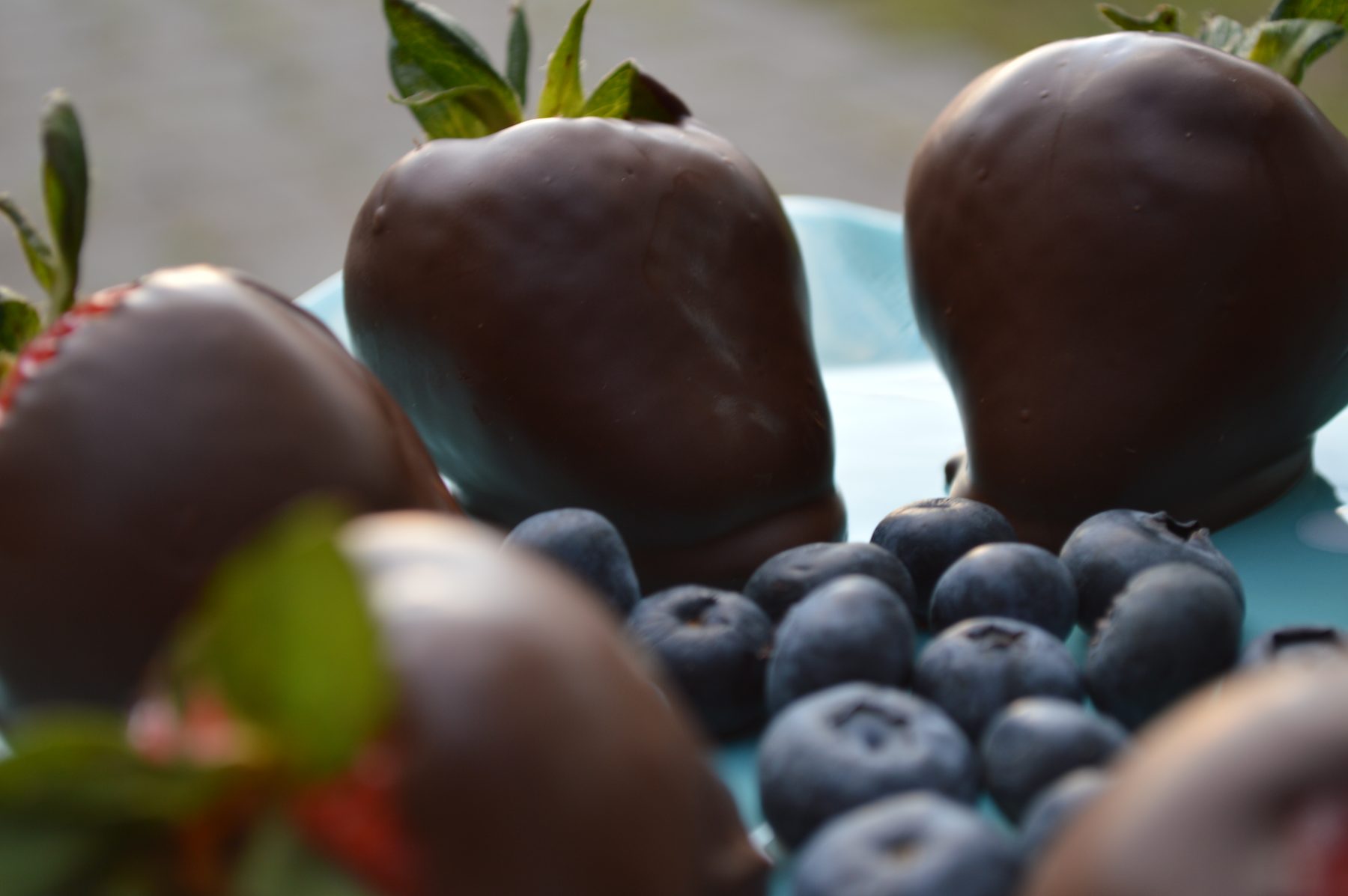 Chocolate covered strawberries and blueberries on a blue plate