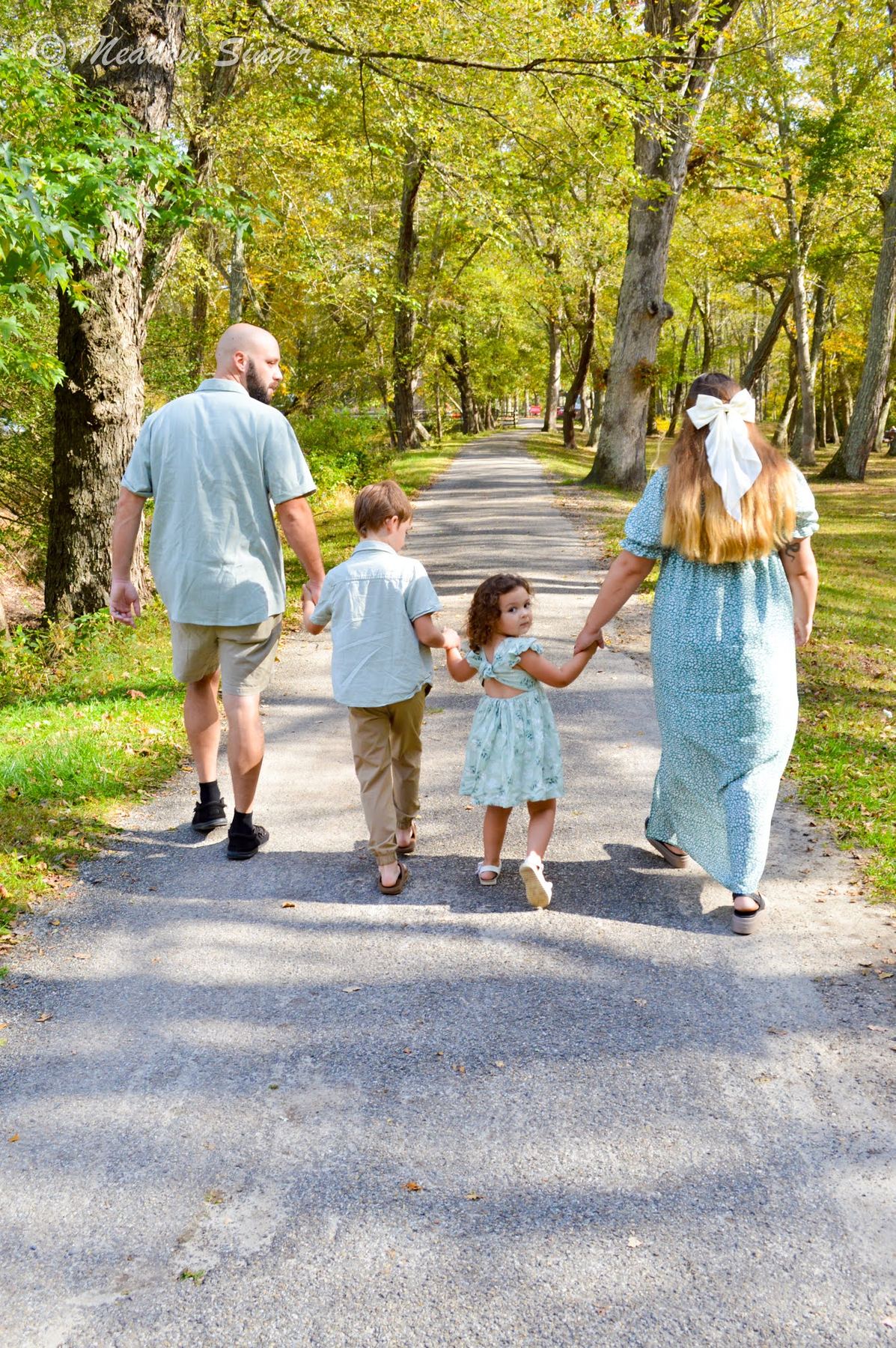 A family of four walking hand in hand down a forest road