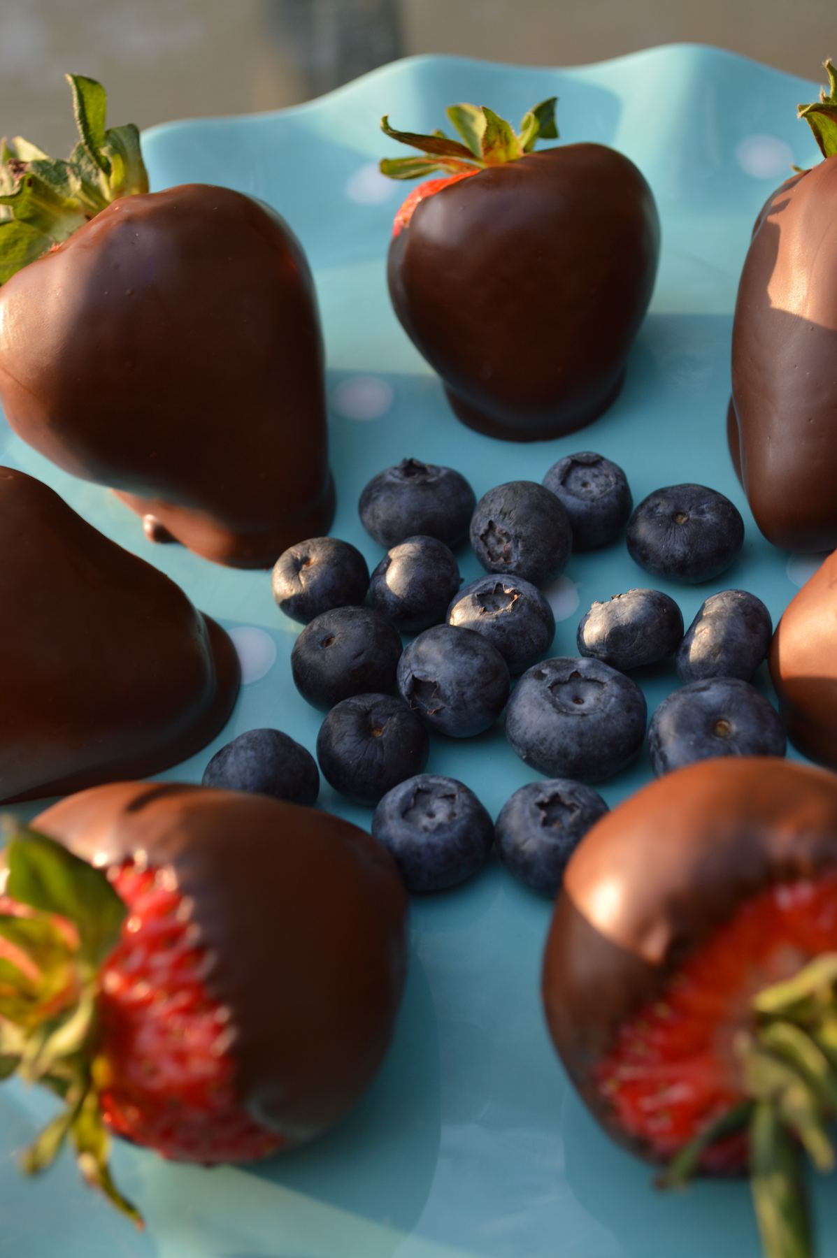 Chocolate covered strawberries and blueberries on a blue plate